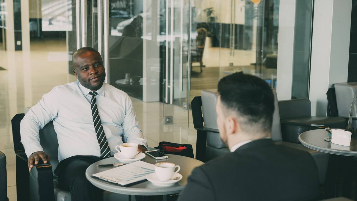 Smiling businessman drinking coffee and discussing financial report of startup with his partner in modern cafe